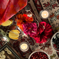 Decorative setting with colorful fabric, candles, and small bowls on a patterned rug.