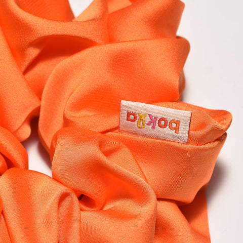 Orange scrunchie with a brand label on a white background