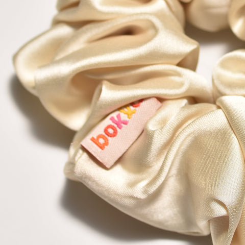 Beige satin scrunchie with a small pink tag on a light gray background