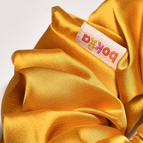 Gold scrunchie with a brand label on a white background