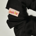 Black scrunchie with a brand label on a light gray background