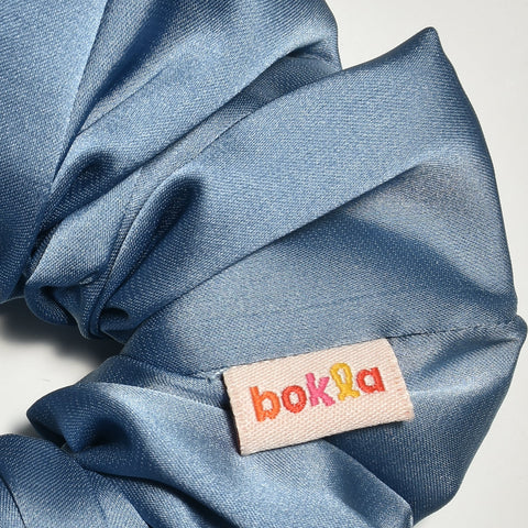 Blue scrunchie with a brand tag on a light gray background