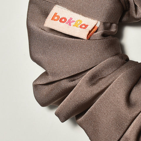 Brown scrunchie with a brand label on a light gray background