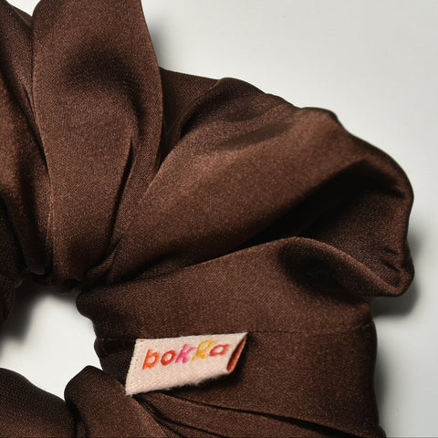 Brown scrunchie with a brand label on a light gray background