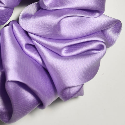 Purple satin scrunchie with a brand label on a light gray background